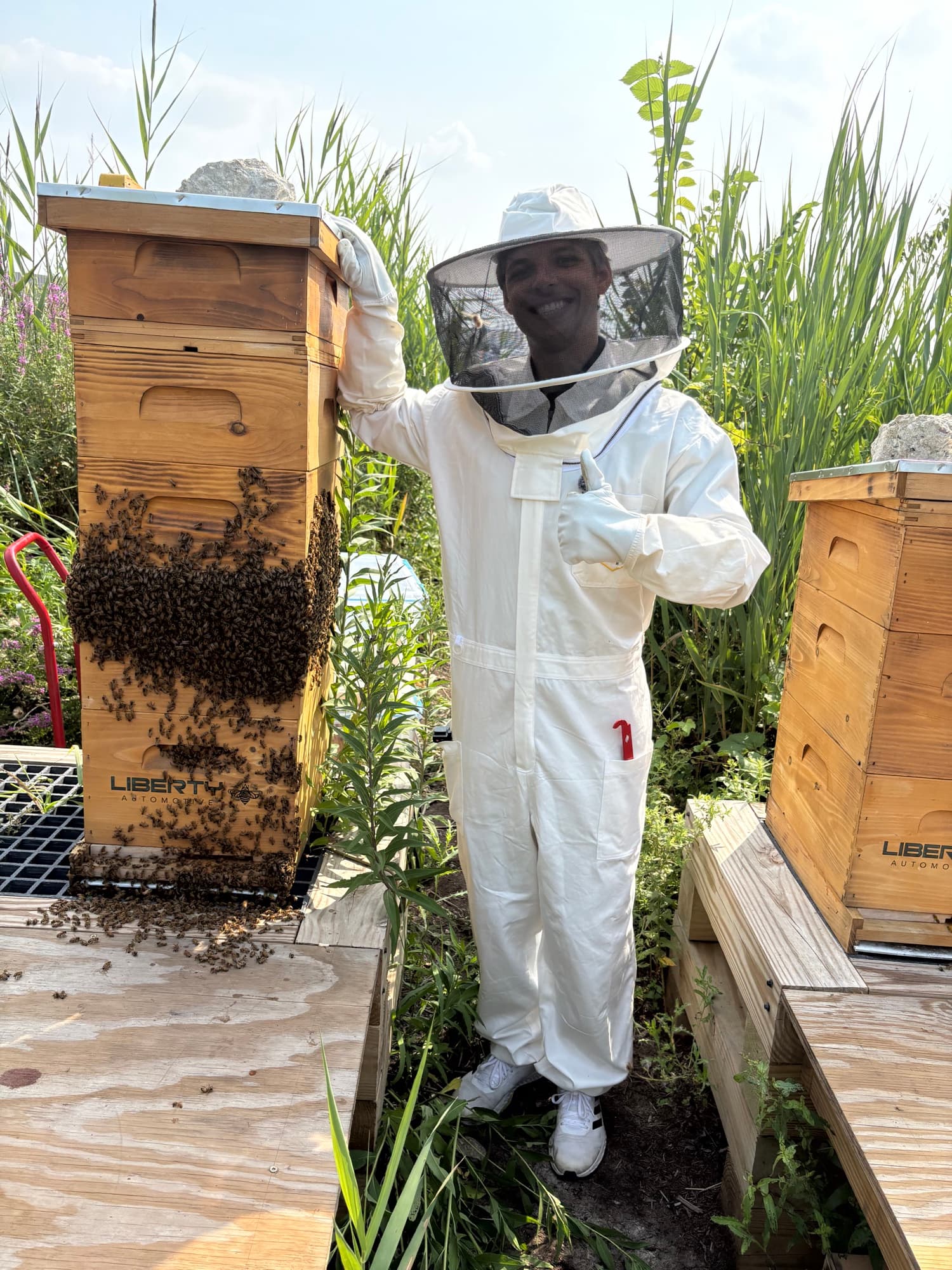 A suited beekeeper gives a thumbs up beside a Liberty Automotive hive